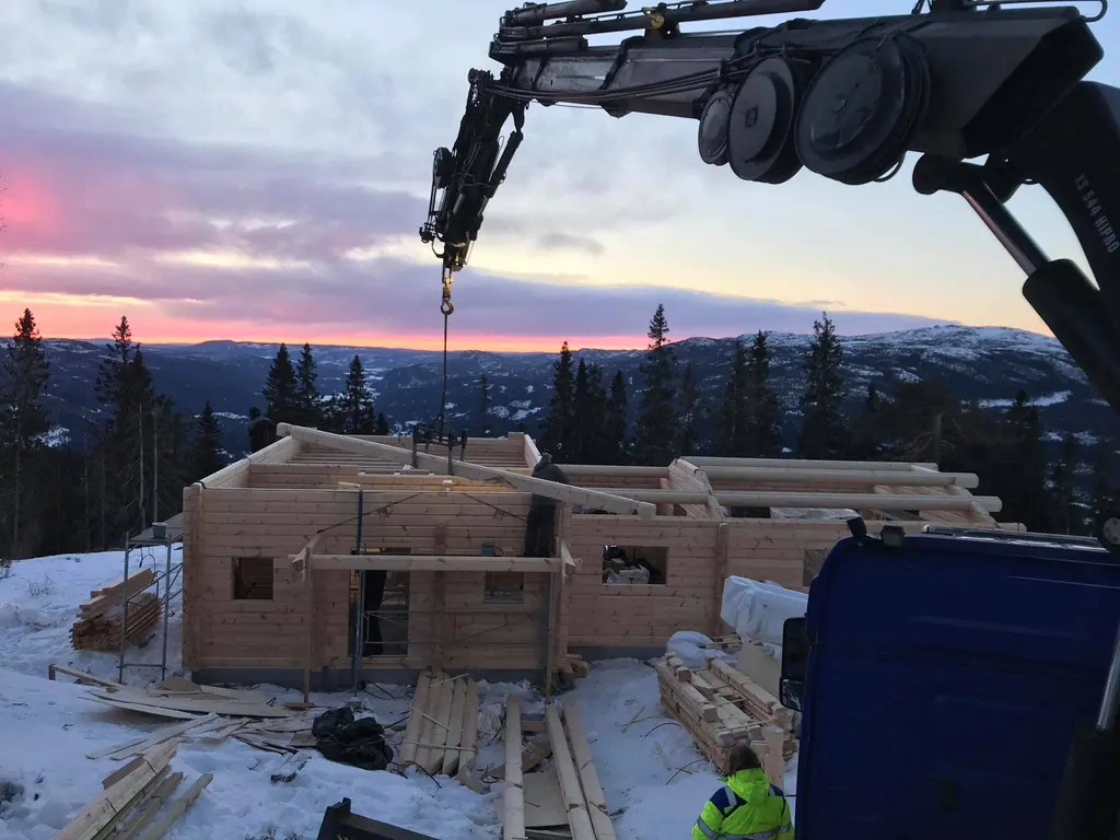 Kranen setter tømmer på en laftehytte i solnedgang